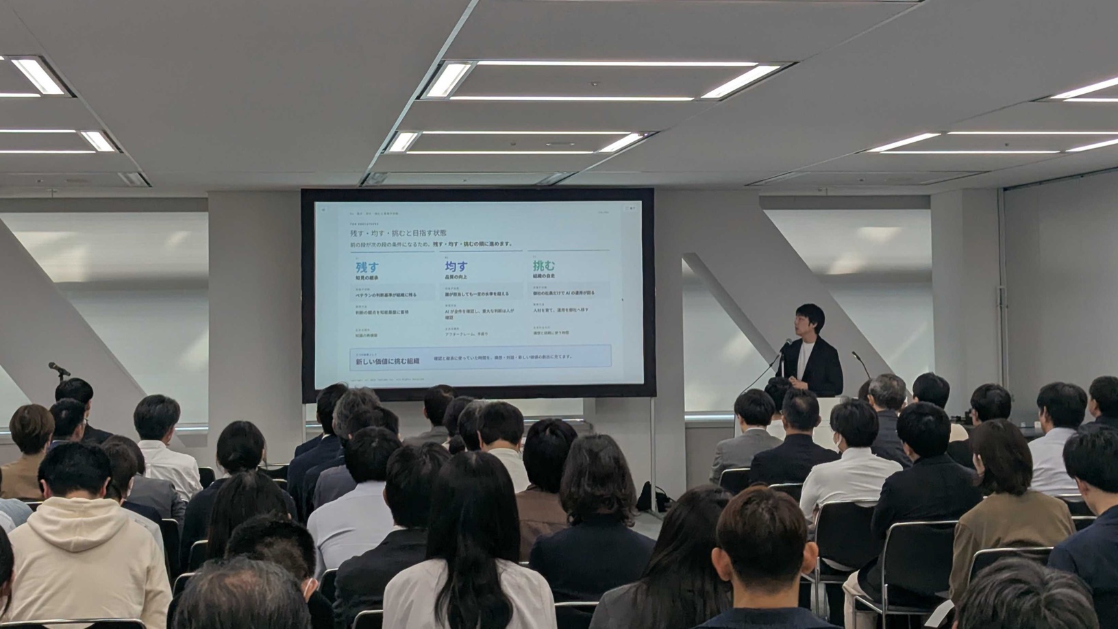 テクニカルフォーラムの会場。満席の聴衆の前で、「残す・均す・挑む」のスライドを映して登壇している