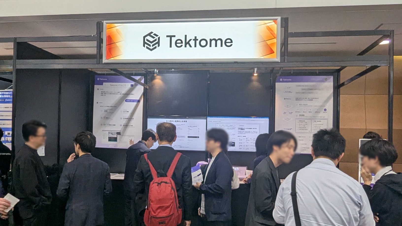 Tektomeのブース。Tektomeのロゴサインの下で来場者がデモ画面を見ている